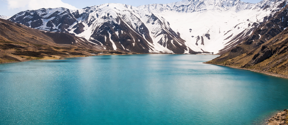 Lago Embalse El Yeso com águas azul-turquesa e montanhas nevadas na Cordilheira dos Andes, Chile
